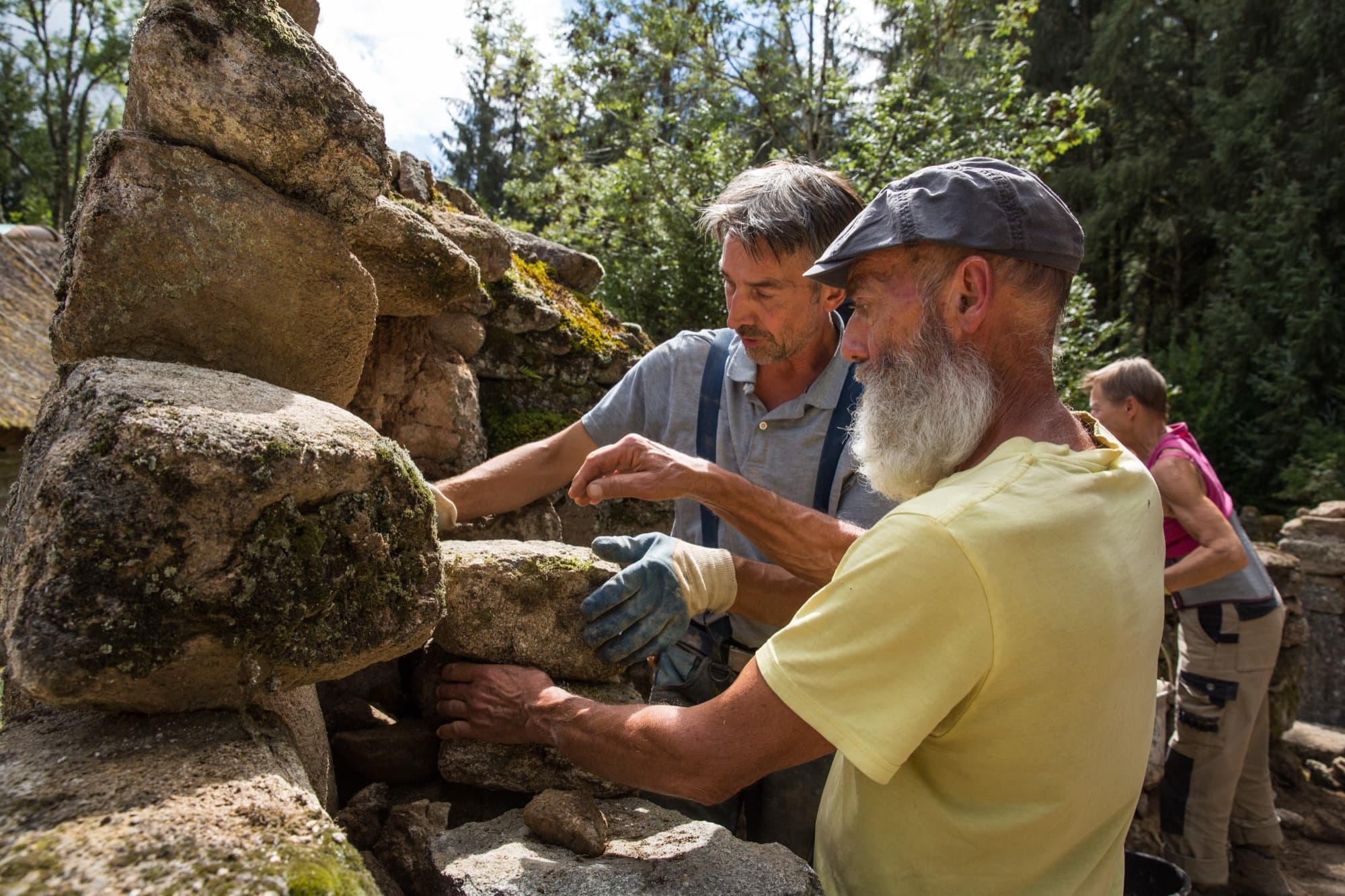 Deux maçons posant une grosse pierre à mains nues sur un mur ancien