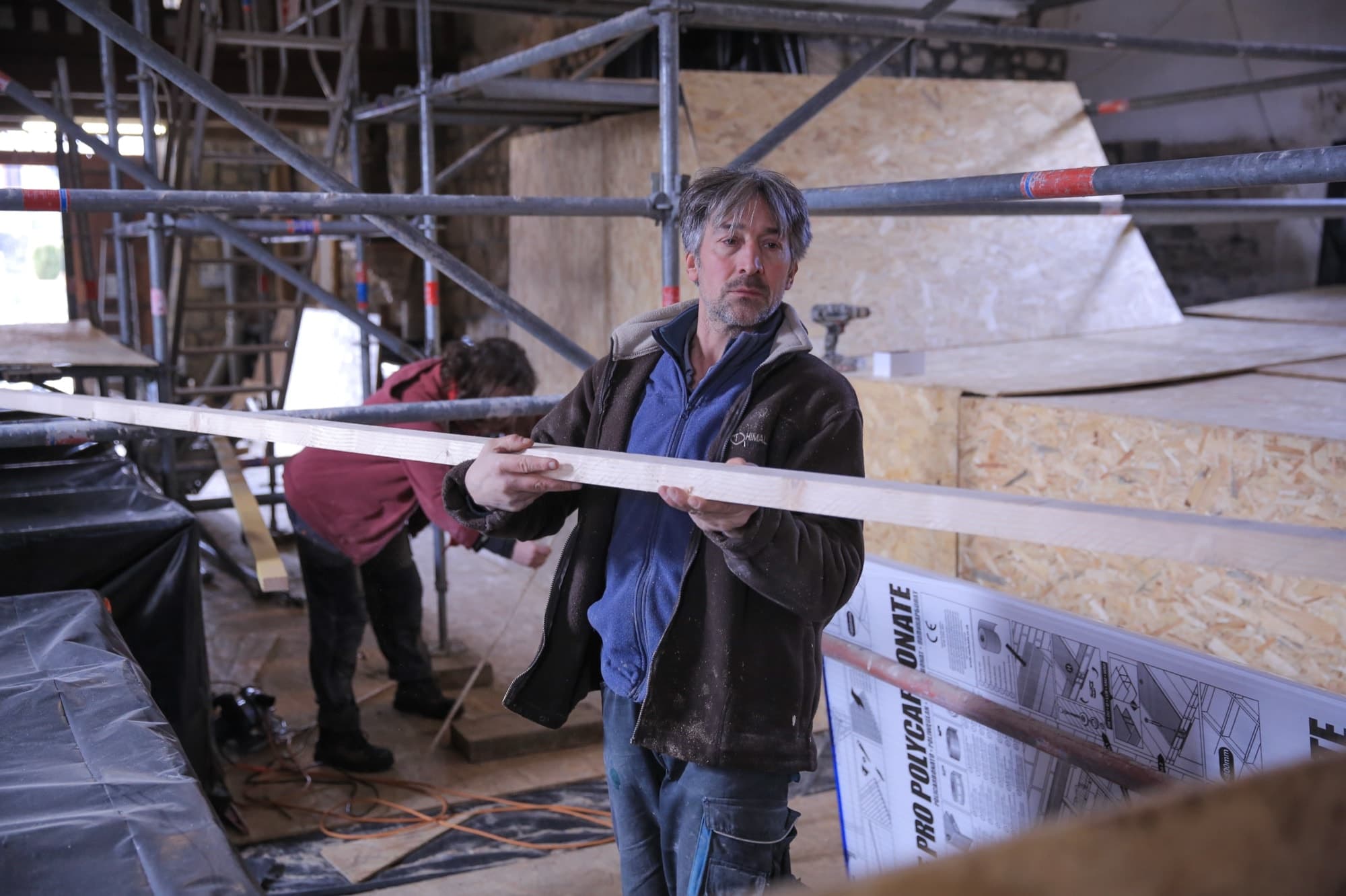Laurent ajustant une planche de bois sur un chantier intérieur